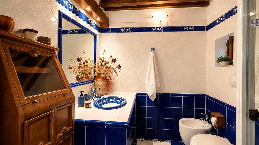 Bathroom with blue handcrafted tiles, traditional washbasin and wooden beams at Vicolo di Sorano