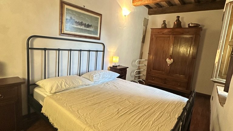 Double bedroom with iron bed and exposed wooden beams at Vicolo di Sorano in Tuscany